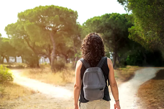 Frau mit Rucksack steht vor einer Weggabelung