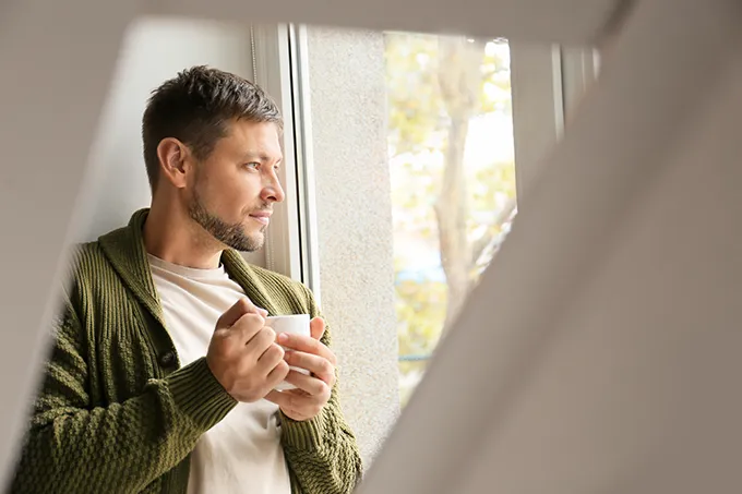 Mann mit Teetasse blickt nachdenklich aus dem Fenster