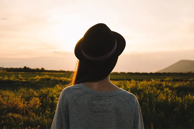 Frau mit Hut schaut zum Sonnenuntergang